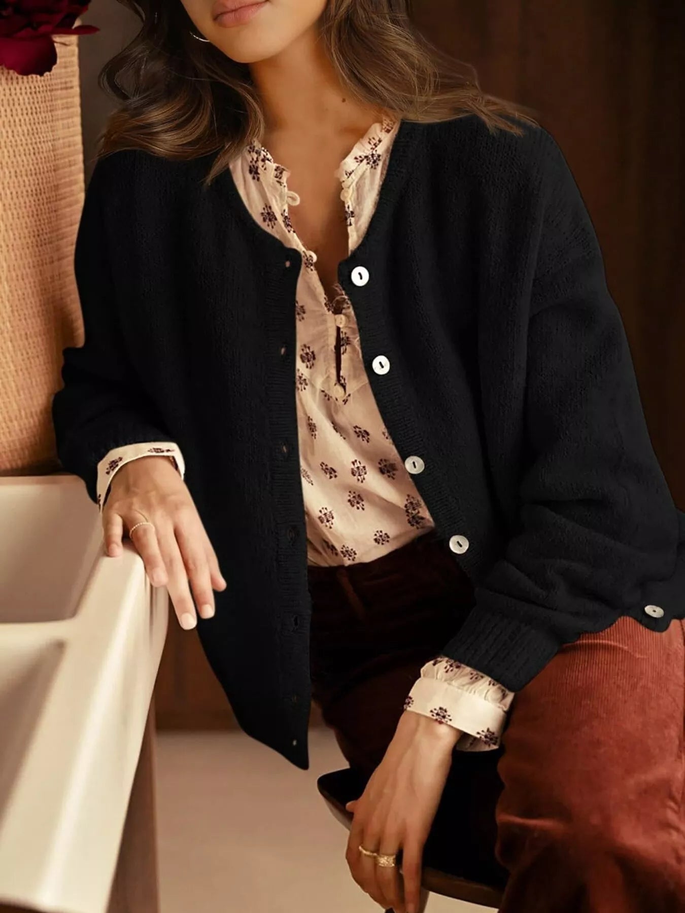 Open black button down cardigan worn over a floral blouse while seated indoors