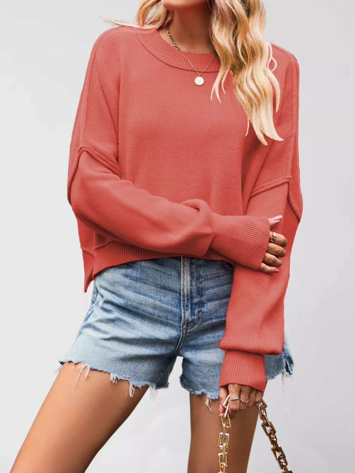Front view of a coral crew neck dropped shoulder sweater with ribbed cuffs worn with denim shorts.