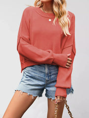Front view of a coral crew neck dropped shoulder sweater with ribbed cuffs worn with denim shorts.