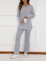 Women's blue and white striped long sleeve top and wide leg pants set, standing against white wall, holding a cup.