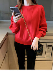 Front view of a red batwing sleeve knit top with vertical seams, holding a phone indoors.