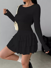 Black long sleeve mini dress worn in a side view showing the ruched waist and tiered ruffle skirt