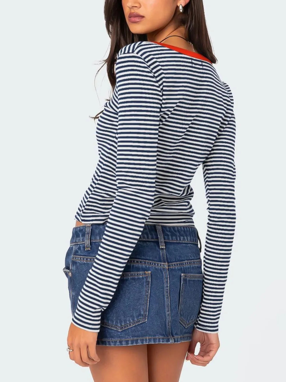 Back view of navy and white striped long sleeve t shirt with orange red neckline trim worn on model