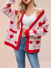 Pink knit cardigan with red hearts and red trim worn open off shoulder