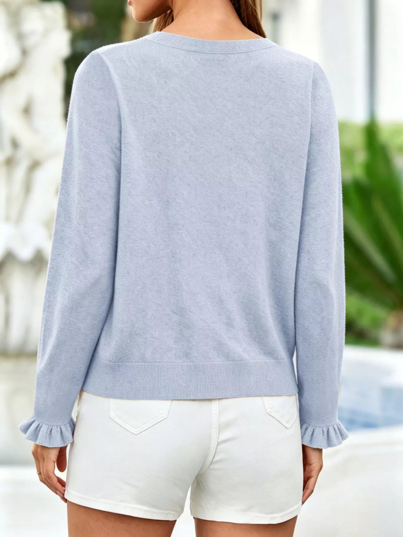 Back view of light blue ruffle trimmed knit cardigan with ruffled cuffs and white shorts