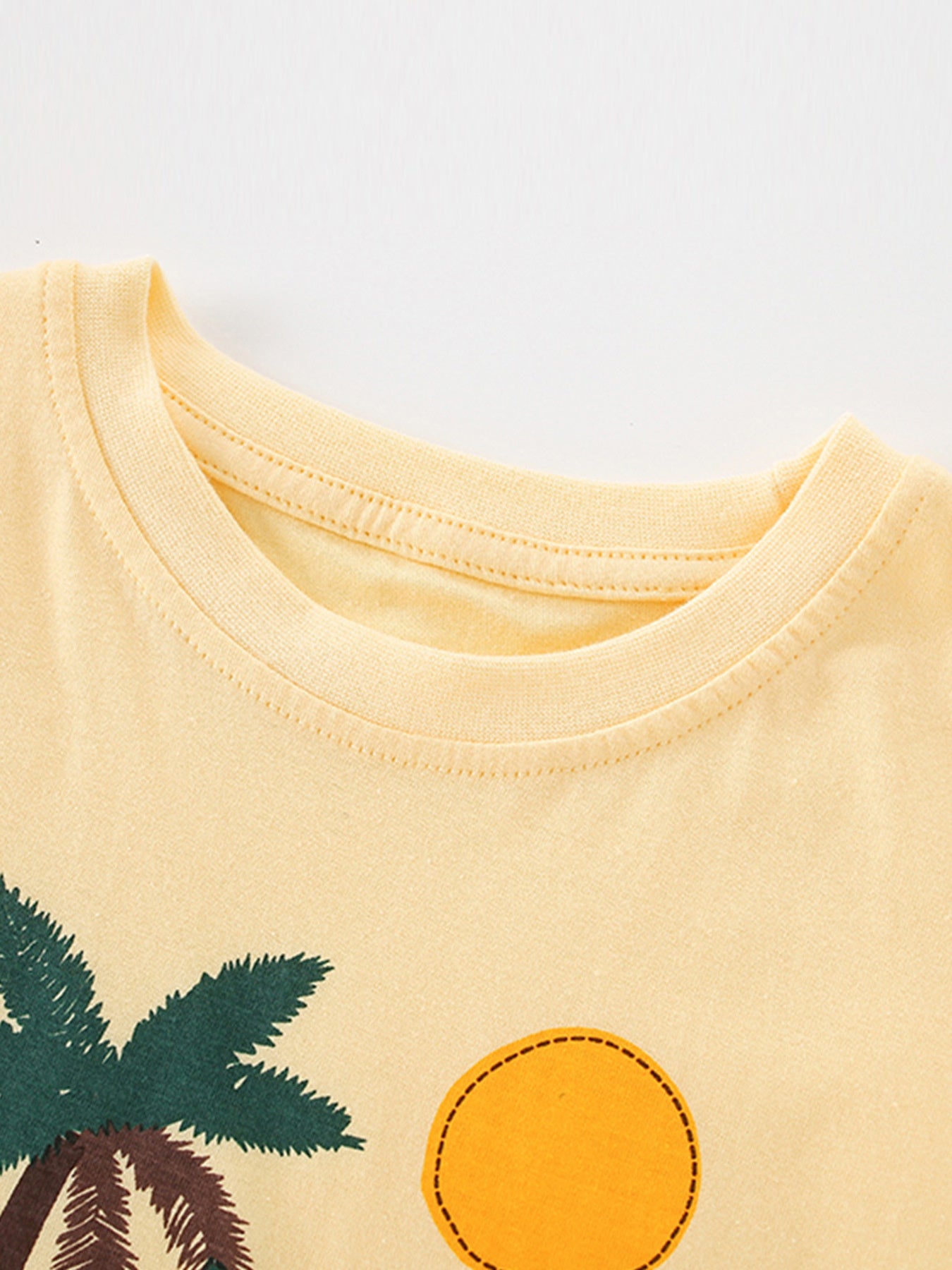 Close-up of the pastel yellow ribbed neckline and palm tree and sun graphics on a children's T-shirt