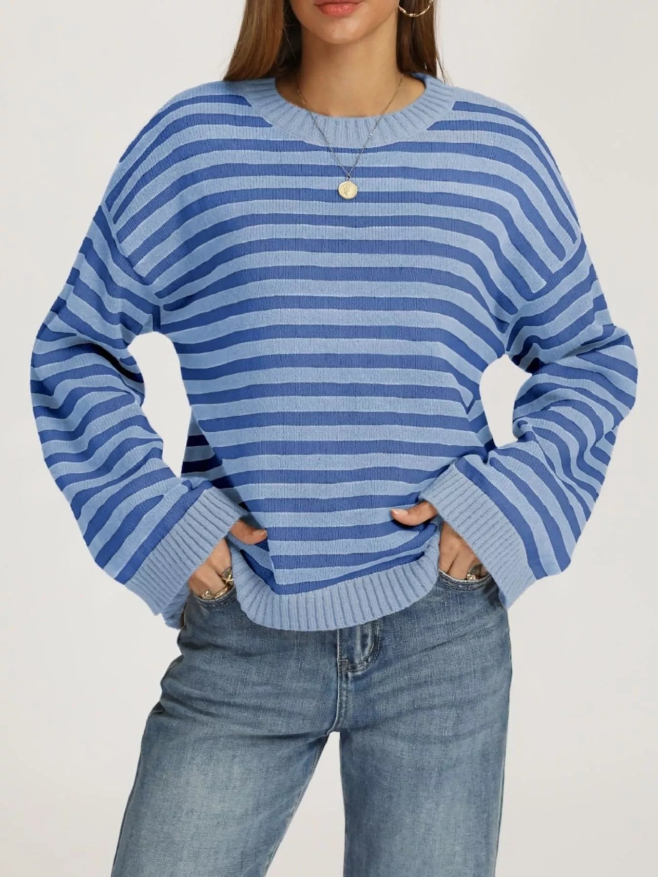 Front view of a light and dark blue striped dropped shoulder sweater with ribbed cuffs worn with jeans.