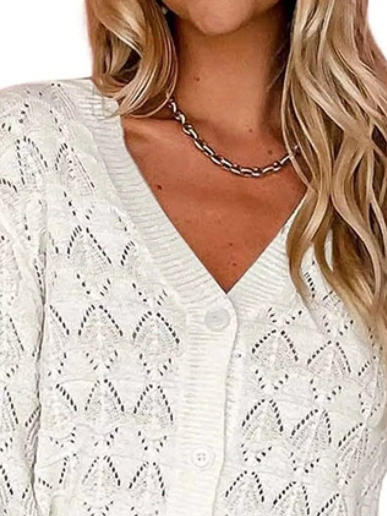 Close view of white openwork knit cardigan showing V neckline and button front.