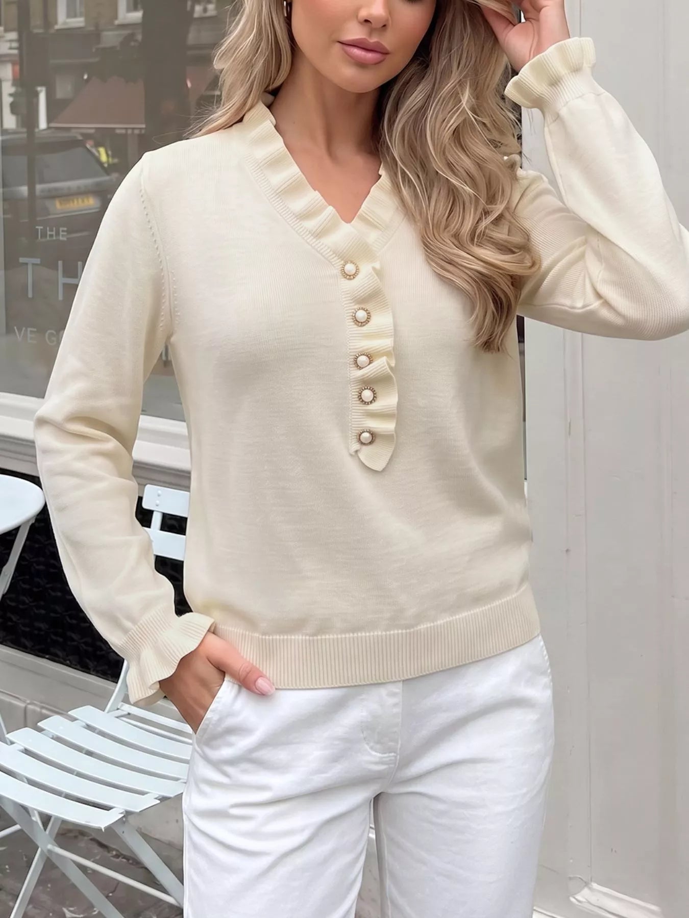 Cream ruffle trim V neck knit top shown front on with hand in pocket