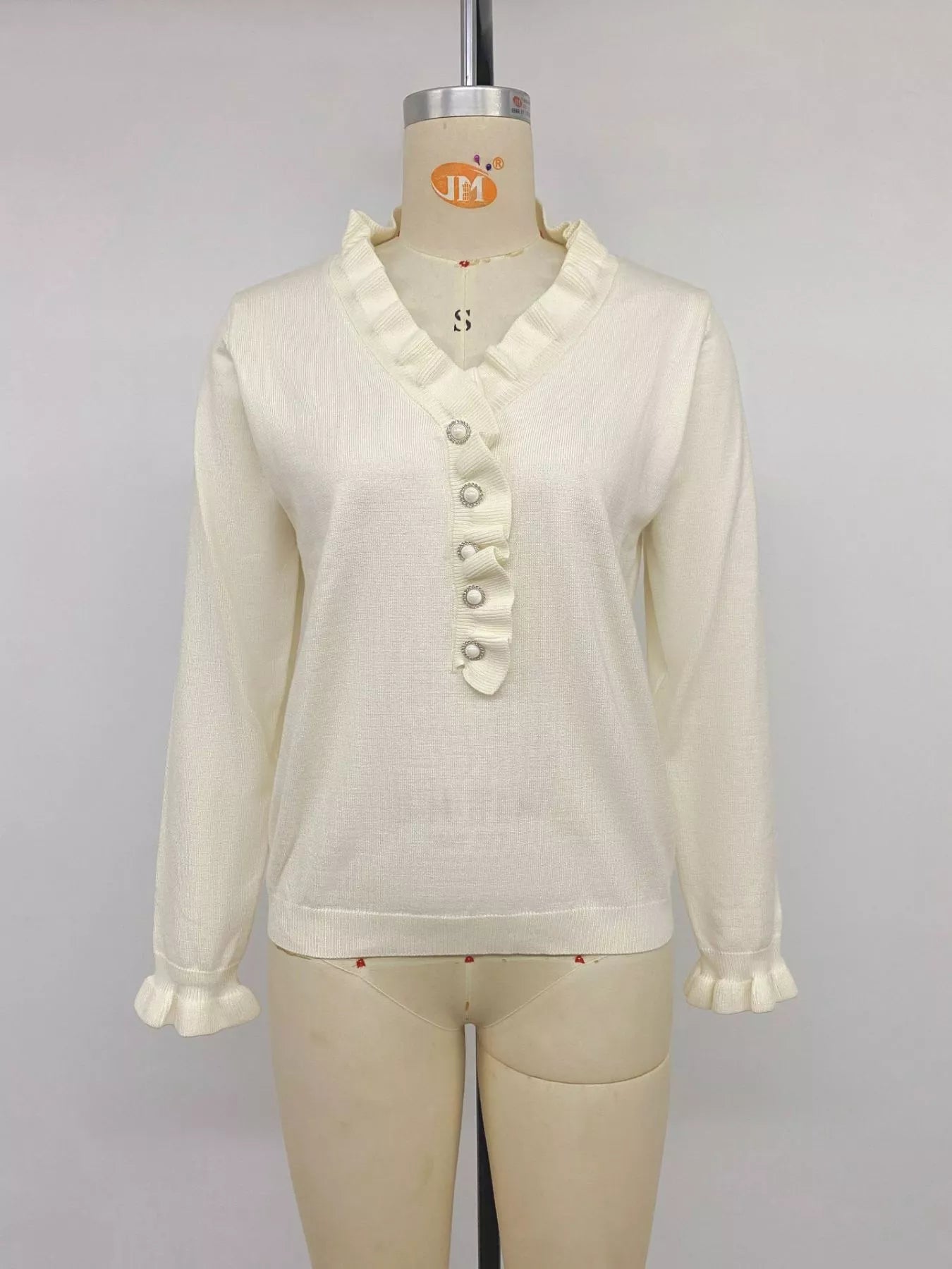 Cream ruffle trim V neck knit top with pearl buttons displayed on mannequin front