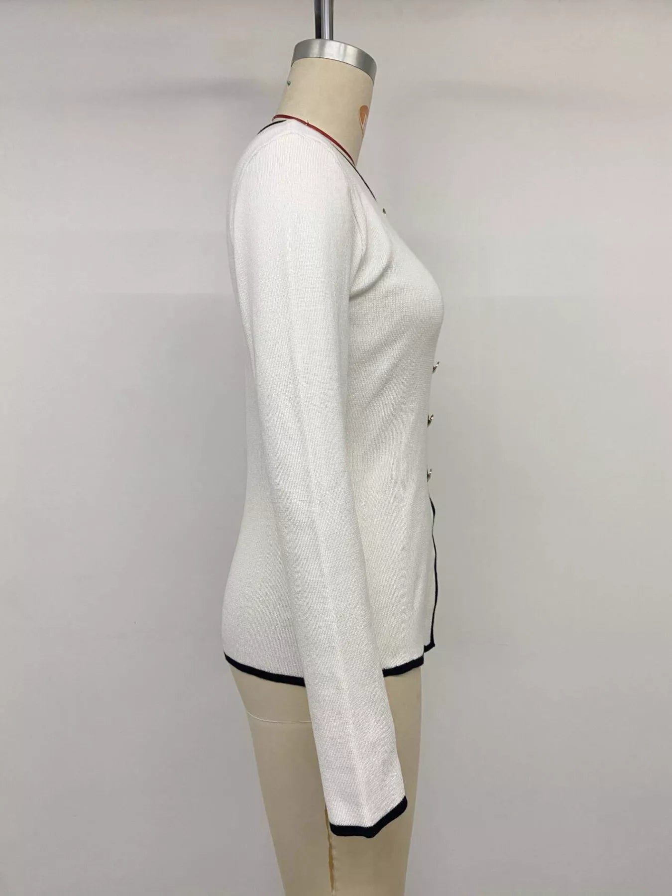 Side view of white knit top on a mannequin, showing long sleeves and black trim.