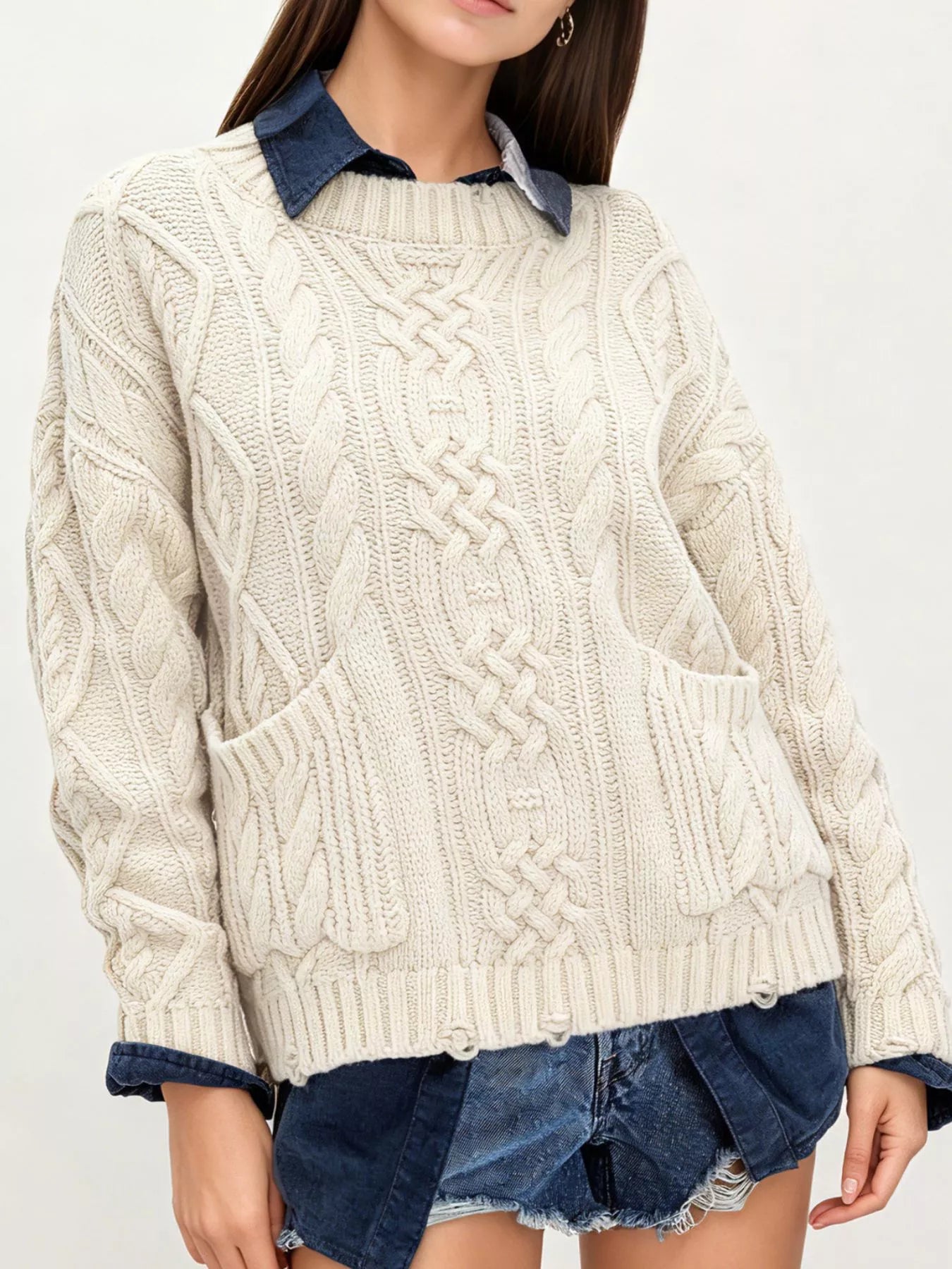 Front view of ivory cable knit sweater with front pockets layered over denim and shorts