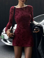 Burgundy floral long sleeve bodycon mini dress worn with jacket over arm, front view near car