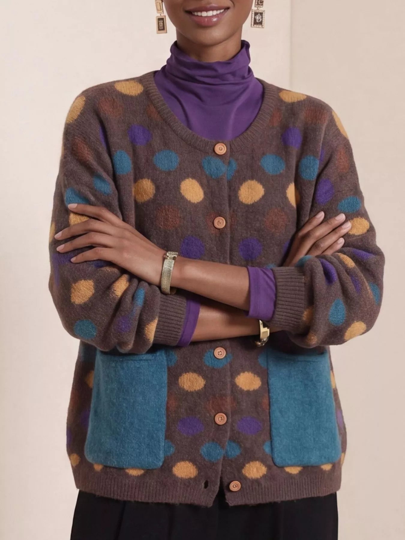 Front view of coffee brown polka dot cardigan with arms crossed and teal pockets
