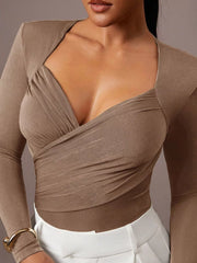 Close cropped front view of khaki ruched surplice bodysuit paired with white trousers