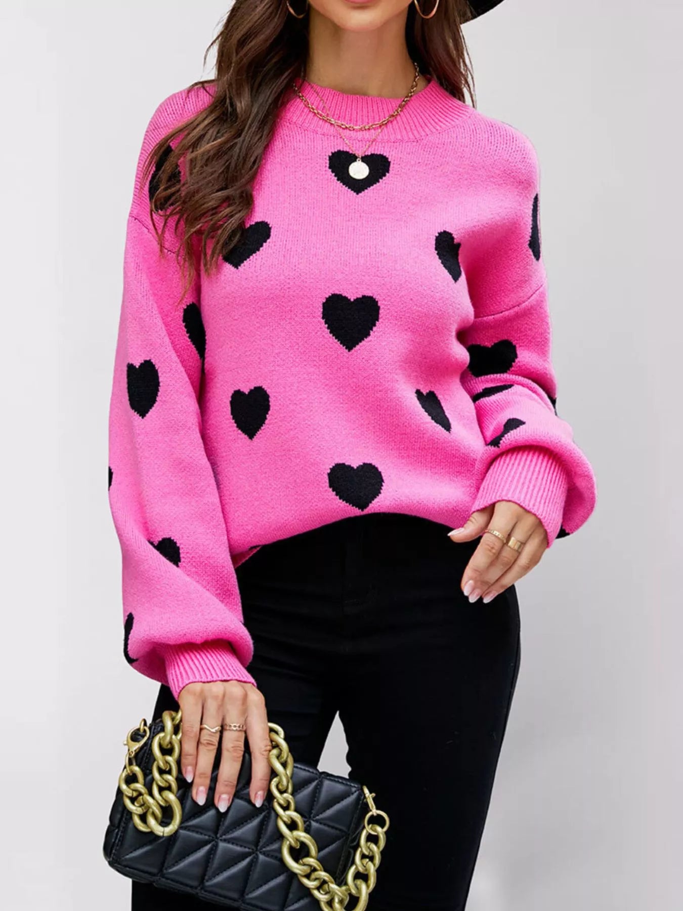 Front view of a hot pink dropped shoulder sweater with black hearts and ribbed cuffs.