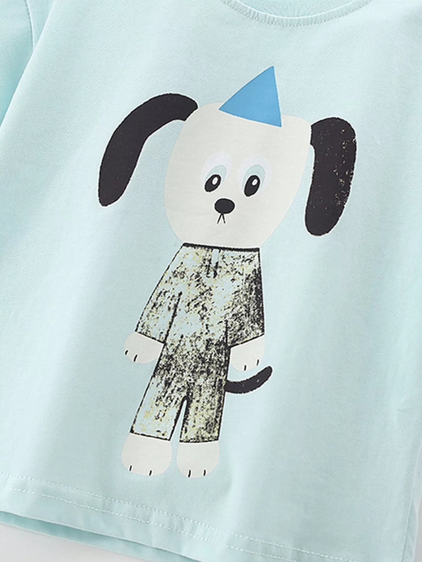 Angled close-up of cartoon dog graphic and hem stitching on mint blue children's t-shirt