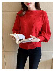 Front view of the red batwing sleeve knit top with vertical seams, holding an open book.