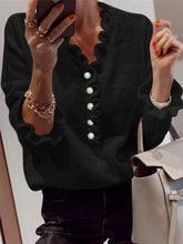 Mirror front view of a black ruffled sweater with pearl buttons and ruffled cuffs