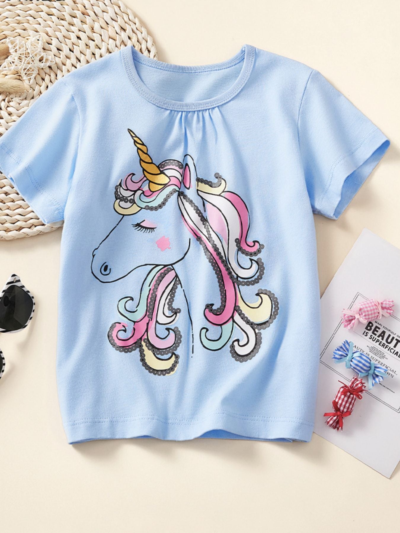 Front view of a pastel blue children's short sleeve tee with a large unicorn head and colorful swirling mane