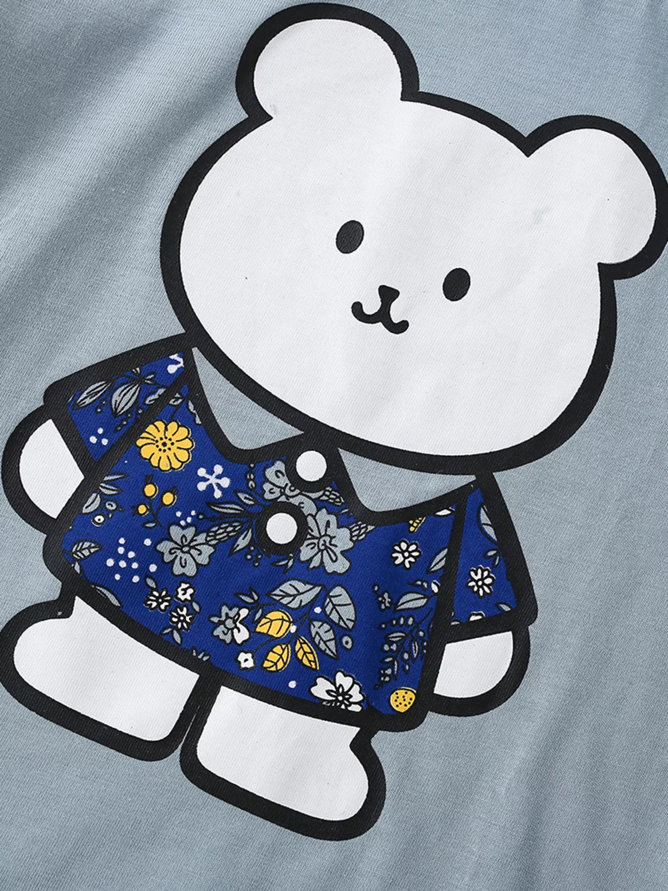 Close-up of white bear graphic wearing a blue floral shirt on light blue children's t-shirt
