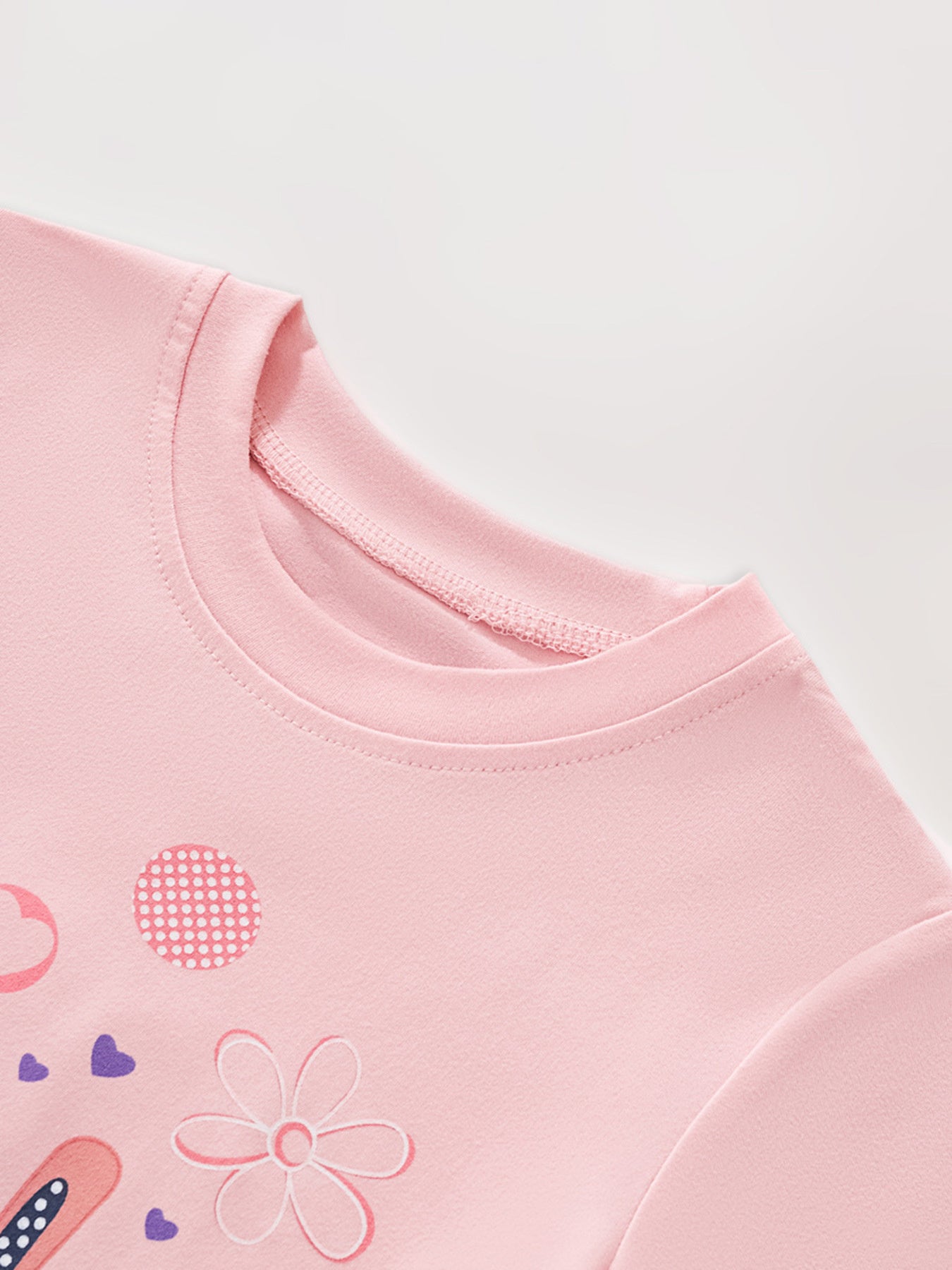 Angled close-up of dusty pink children's tee collar with flower and dotted detail