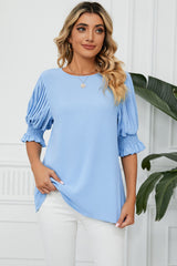 Light blue women's blouse with pleated flounce sleeves and smocked cuffs, shown on a model.