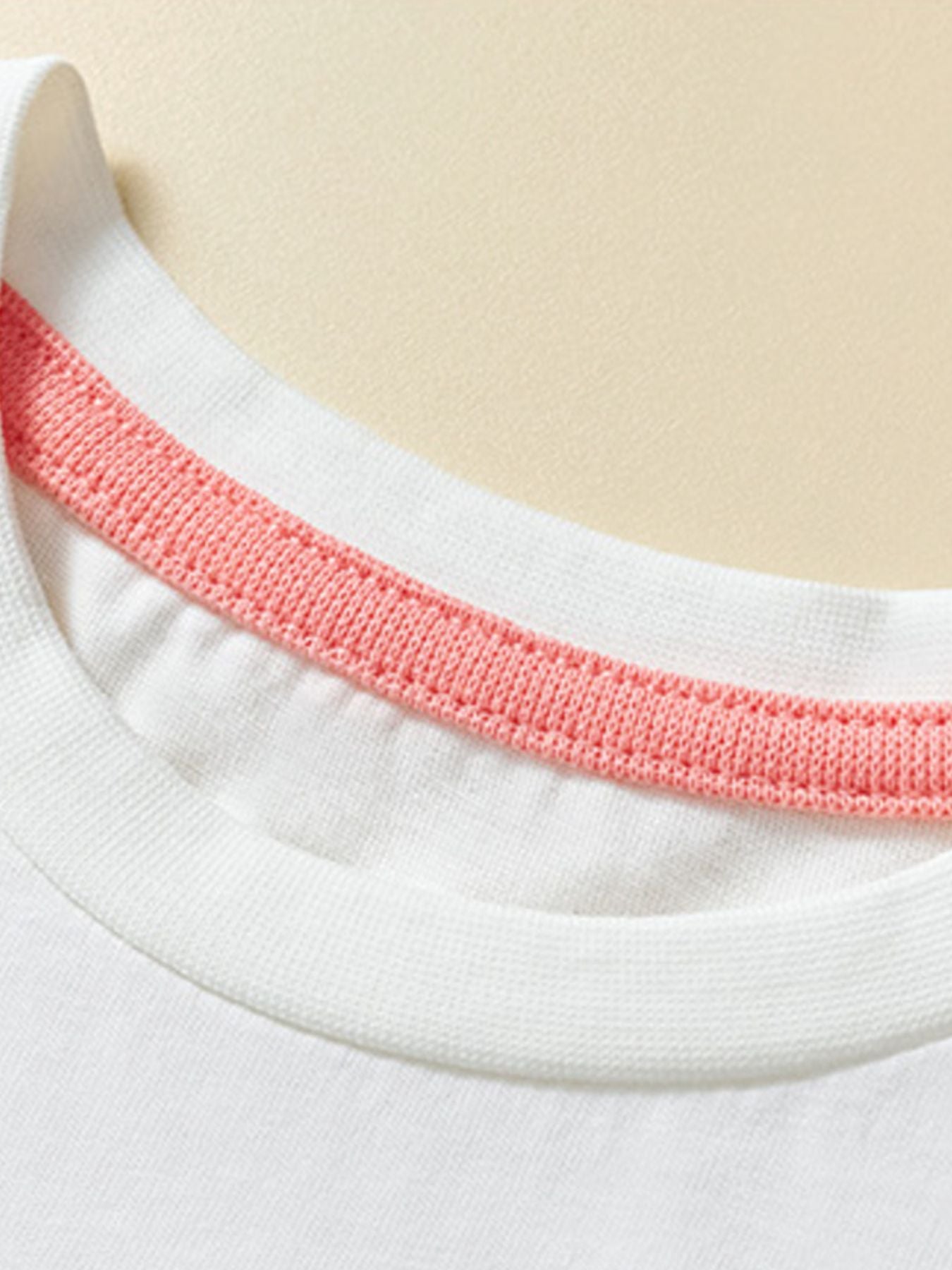 Detail view of the white round neckline with coral inner trim on a children's short sleeve tee