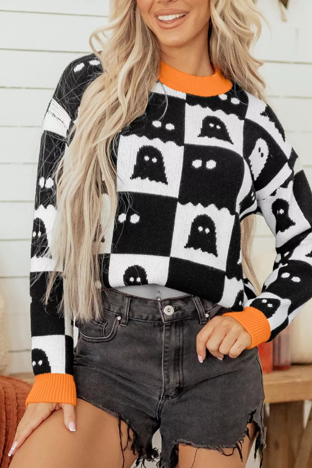 Front view of a black and white checkerboard sweater with ghost pattern and orange trim