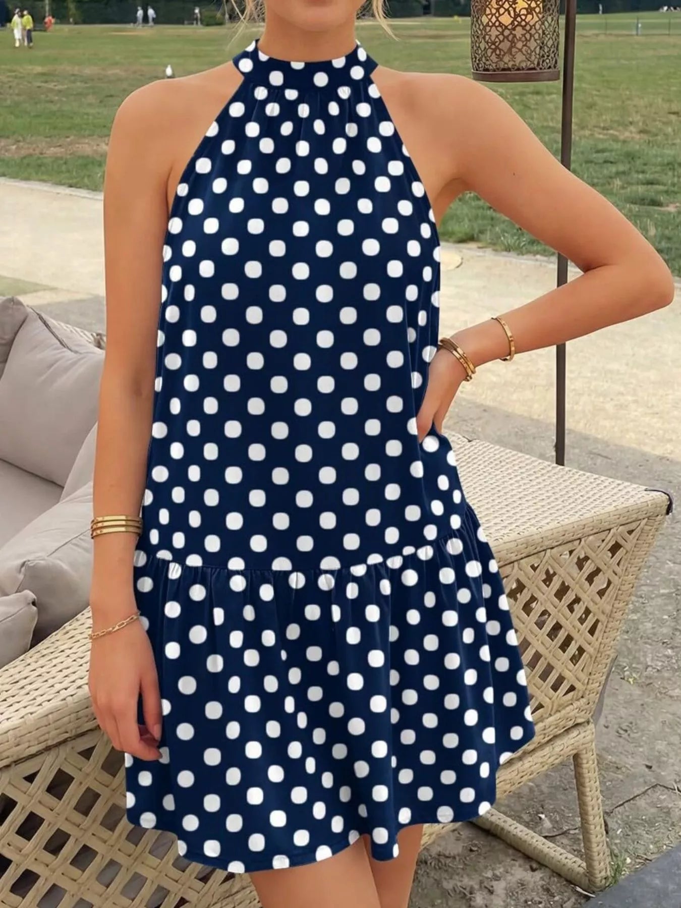 Navy blue polka dot halter neck mini dress worn standing outdoors with ruffled hem