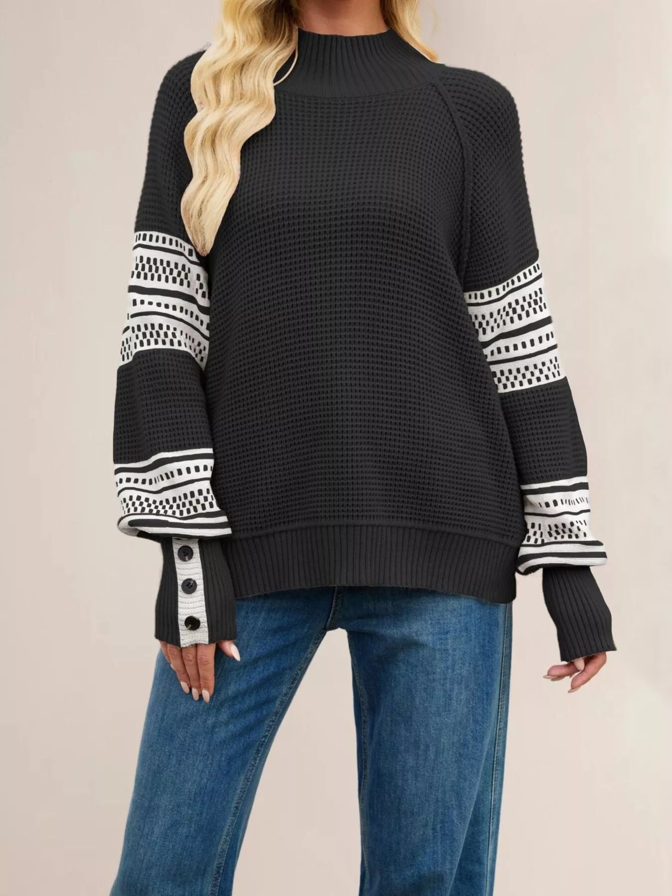 Front view of a black waffle knit sweater with white patterned sleeves and button cuffs.