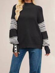 Front view of a black waffle knit sweater with white patterned sleeves and button cuffs.