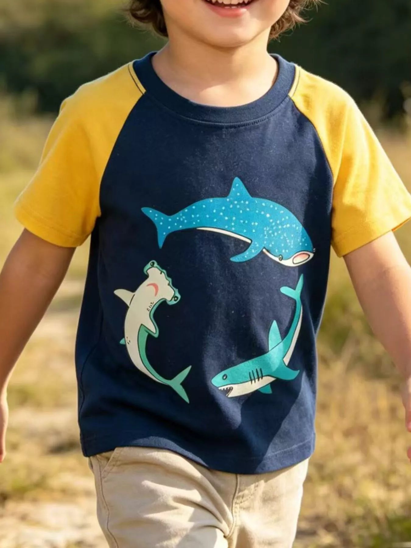 Front view of a dark navy children's raglan t-shirt with yellow sleeves and three shark prints