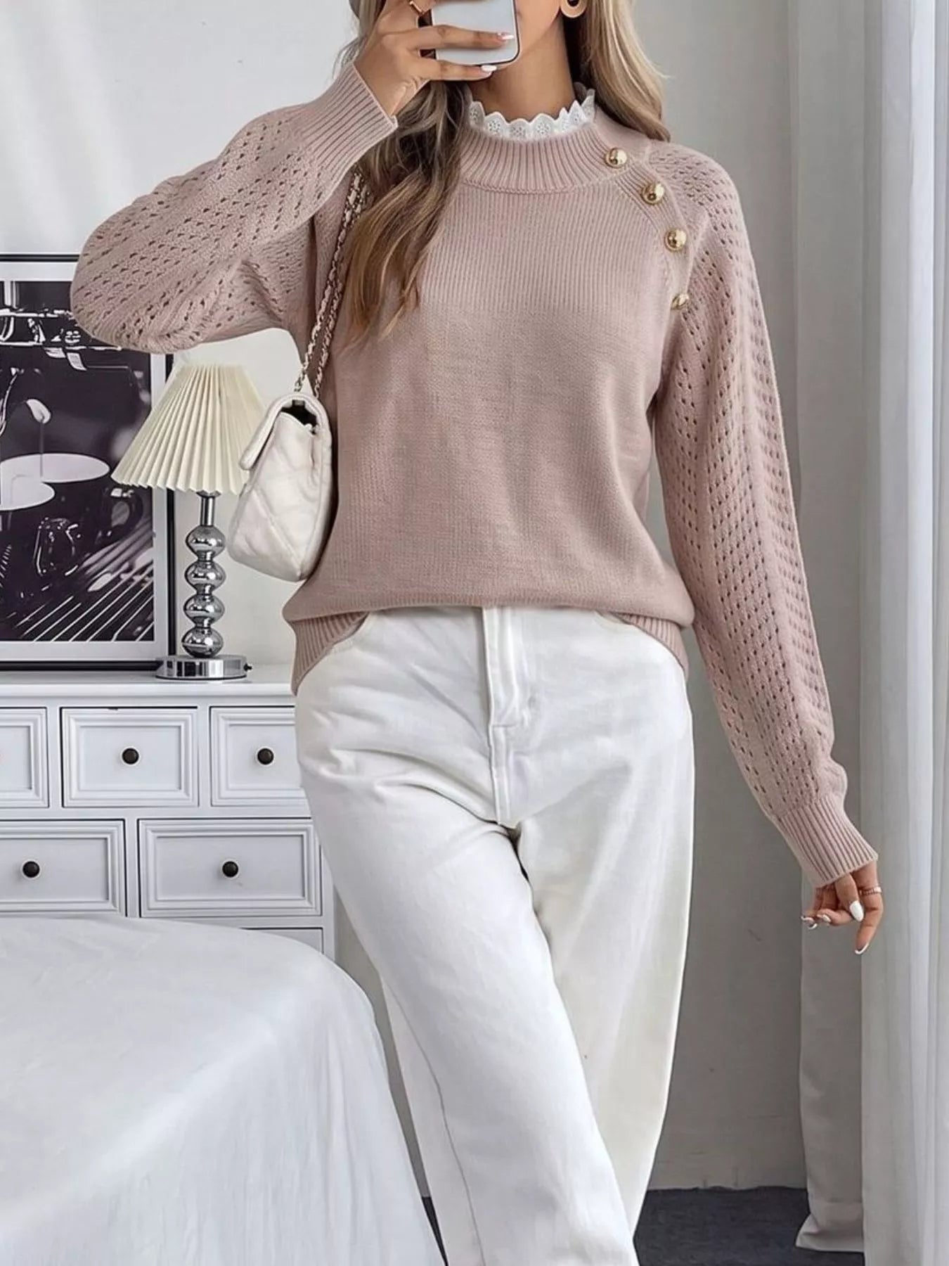 Full length front view of a pink openwork sweater with gold buttons and white trousers