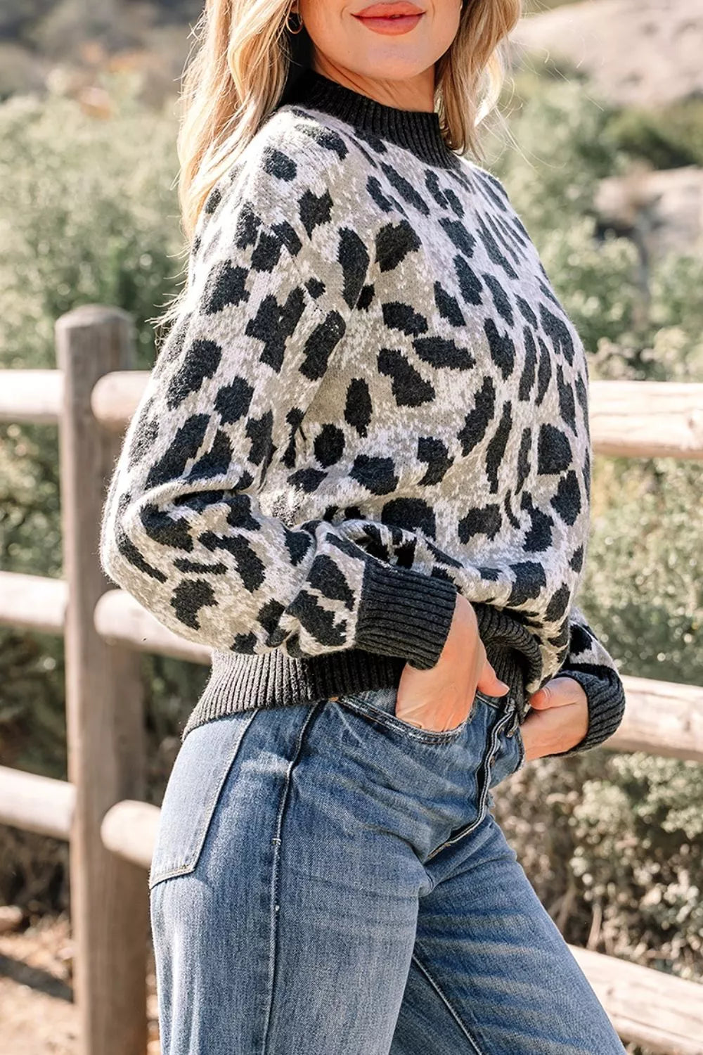Side front view of the gray and black leopard print baggy sweater with ribbed collar, outdoors.