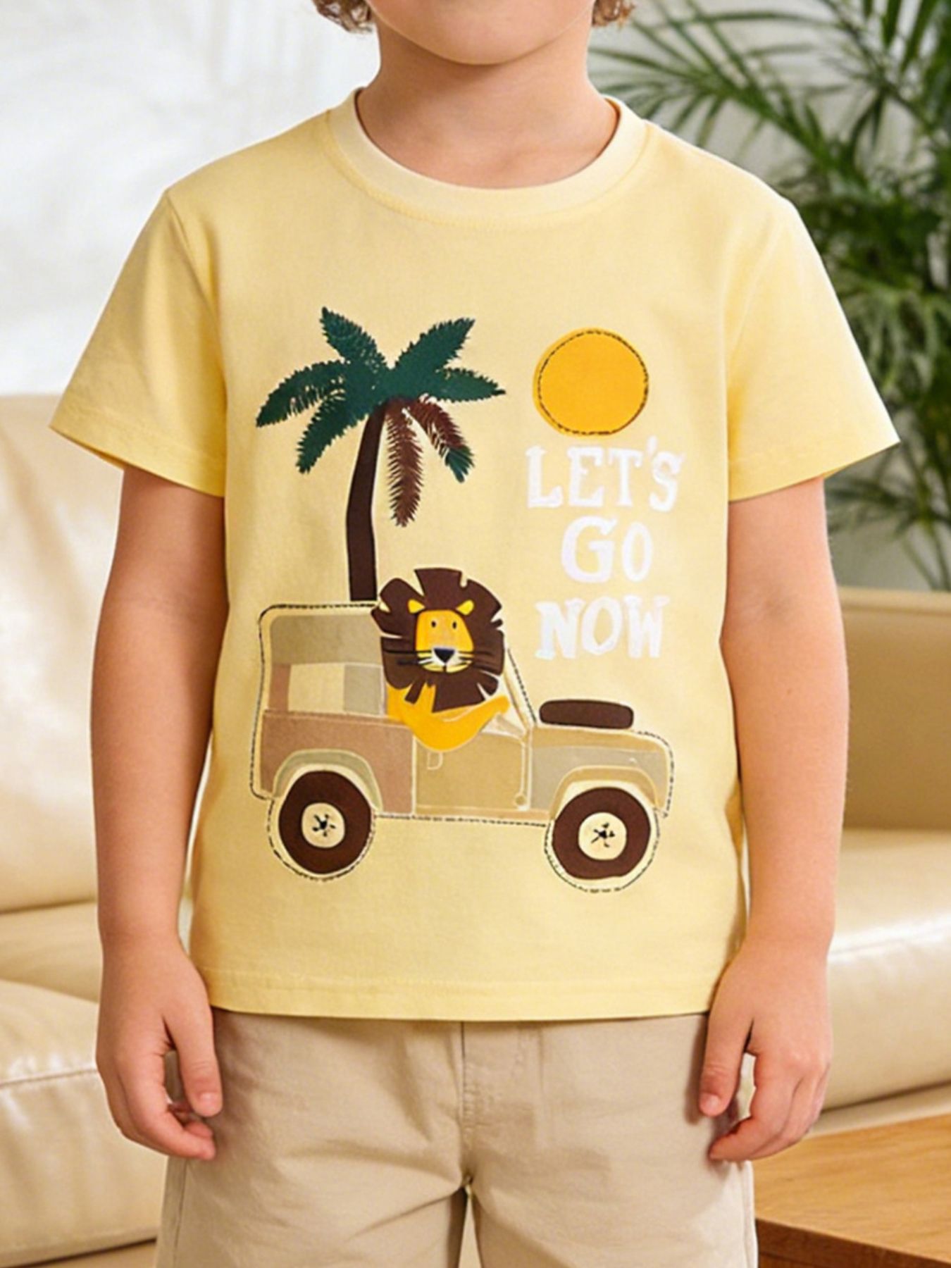 Children's pastel yellow short sleeve T-shirt with a lion driving a safari vehicle graphic, shown worn in front view