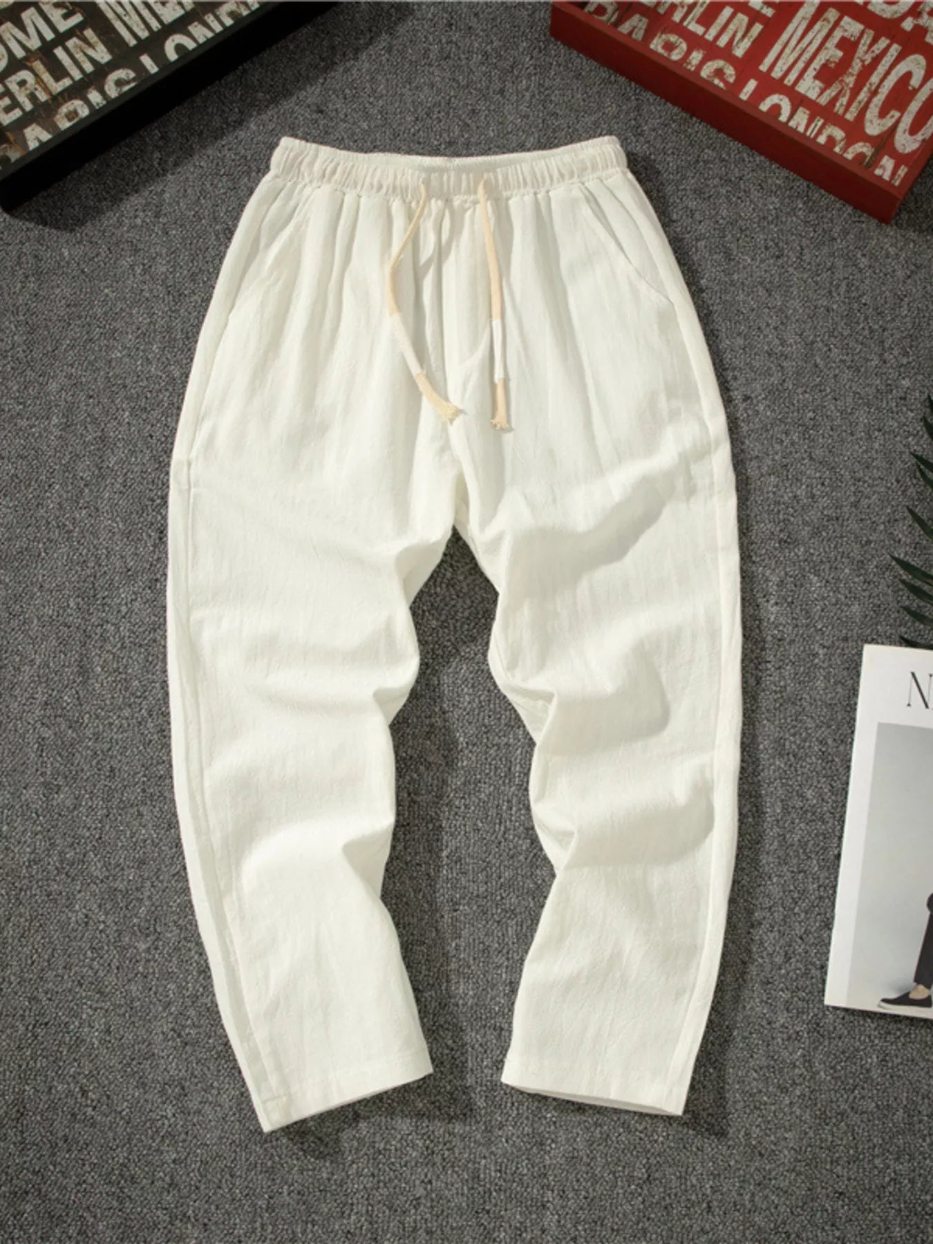 Men's white loose-fit pants with a drawstring waist and pockets.