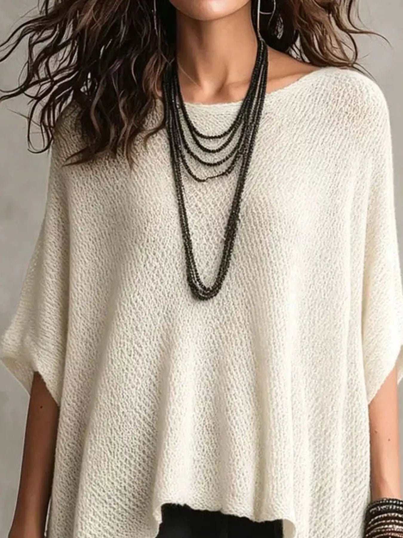 Close front view of a white loose knit cover-up with a wide neckline and layered necklaces