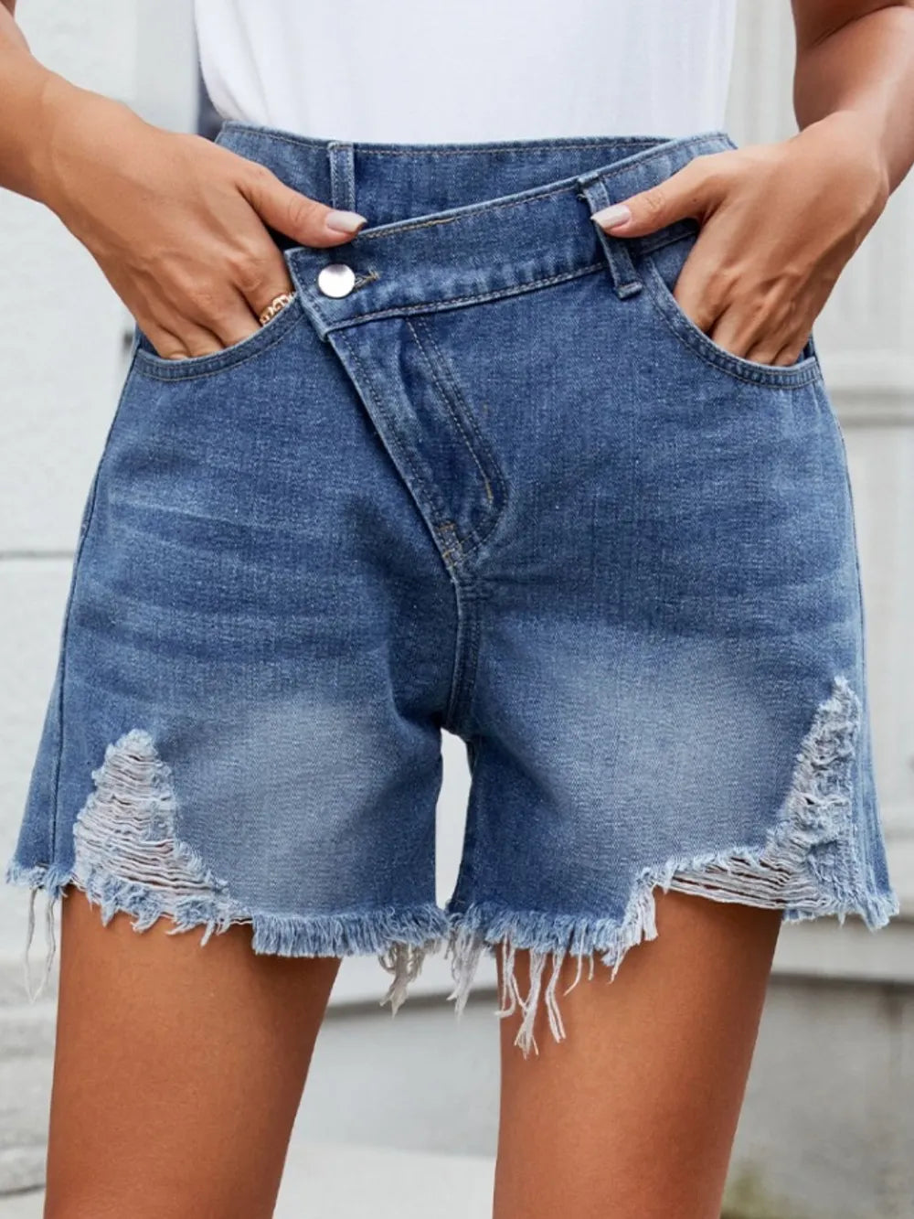 Women's distressed shorts with an asymmetric waist, buttons, pockets, and raw hems.