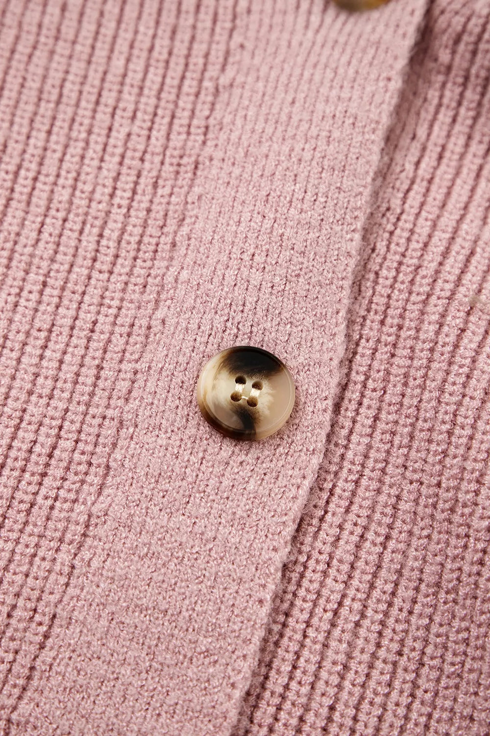 Extreme close-up of a tortoiseshell button on the ribbed dusty pink knit cardigan
