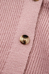 Extreme close-up of a tortoiseshell button on the ribbed dusty pink knit cardigan