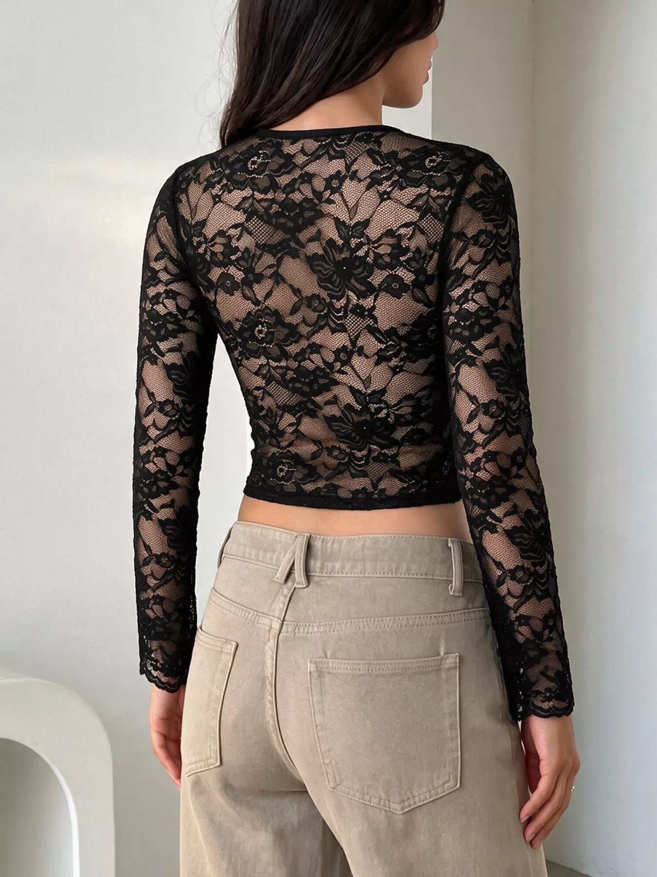 Back view of black floral lace long-sleeve top with cropped hem, worn with beige pants