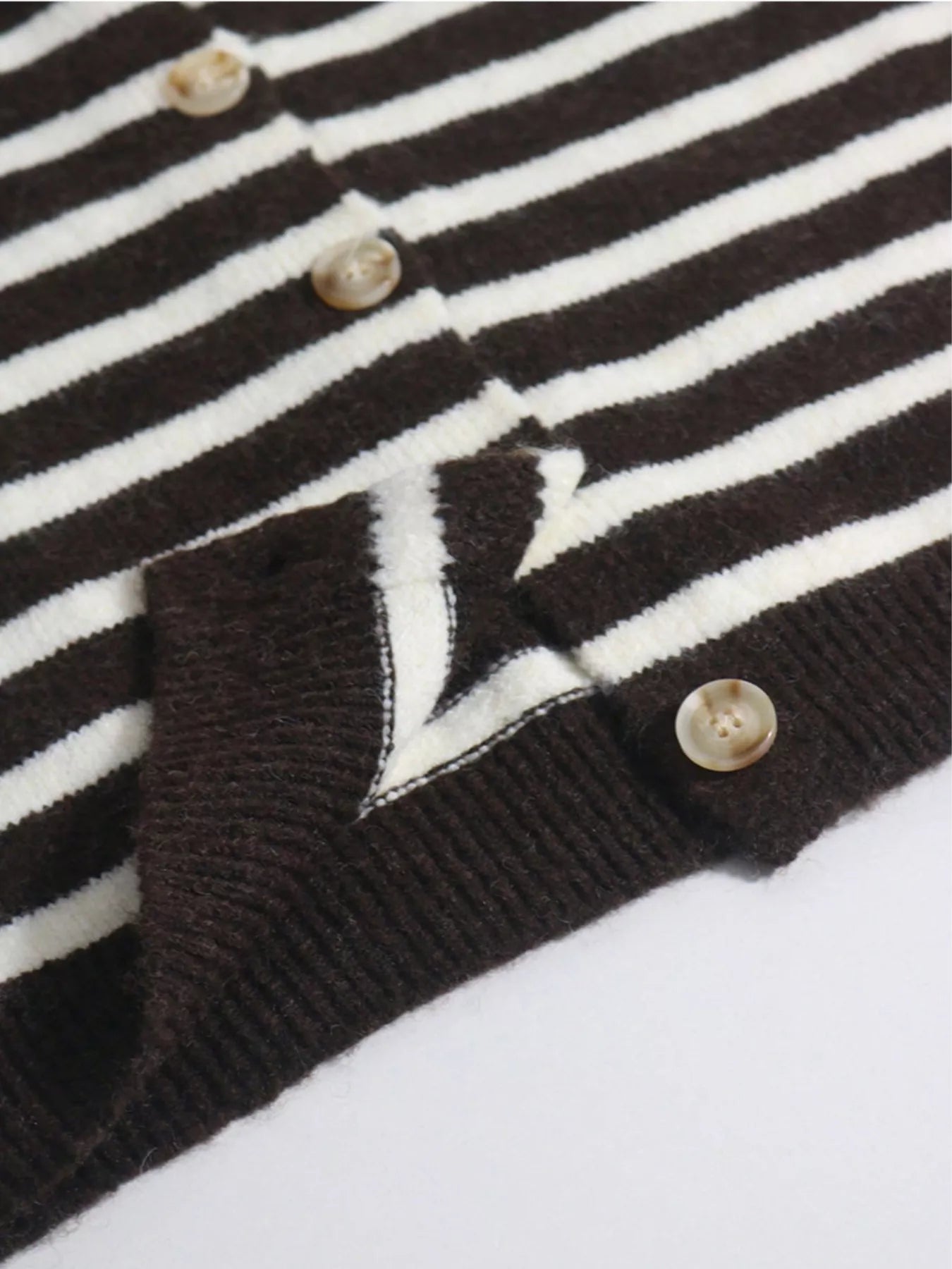 Close up detail of brown and white striped cardigan buttons and ribbed hem on flat surface