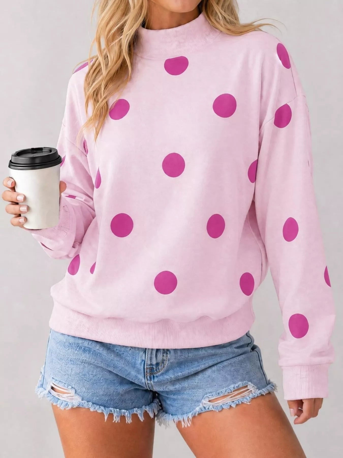 Front view of pink mock neck oversized sweatshirt with magenta polka dots holding a cup