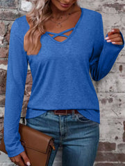 Blue long-sleeve top featuring a crisscross V-neckline, modeled with jeans against a brick wall.