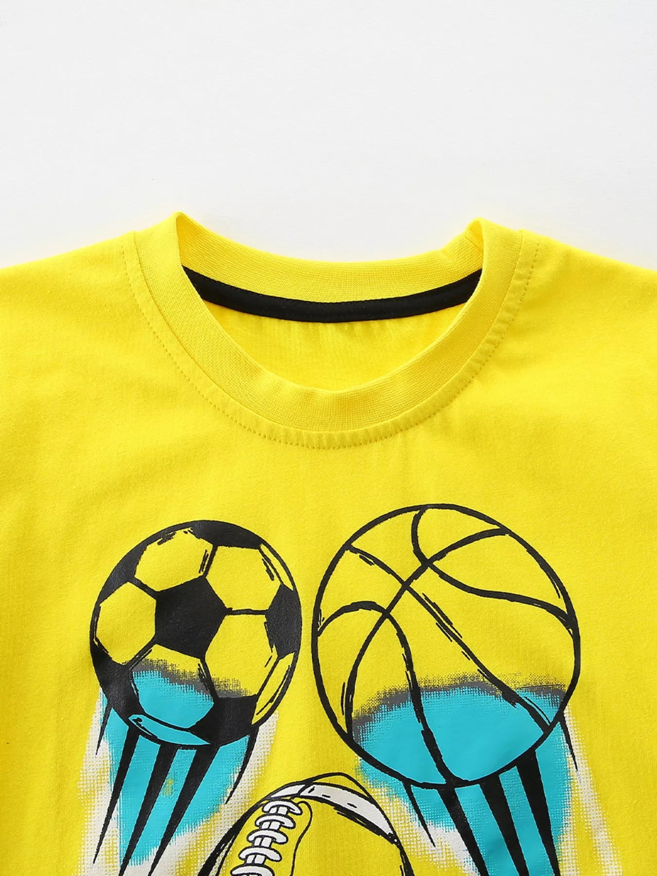 Close up of canary yellow children's t-shirt round neckline with black inner trim and ball prints