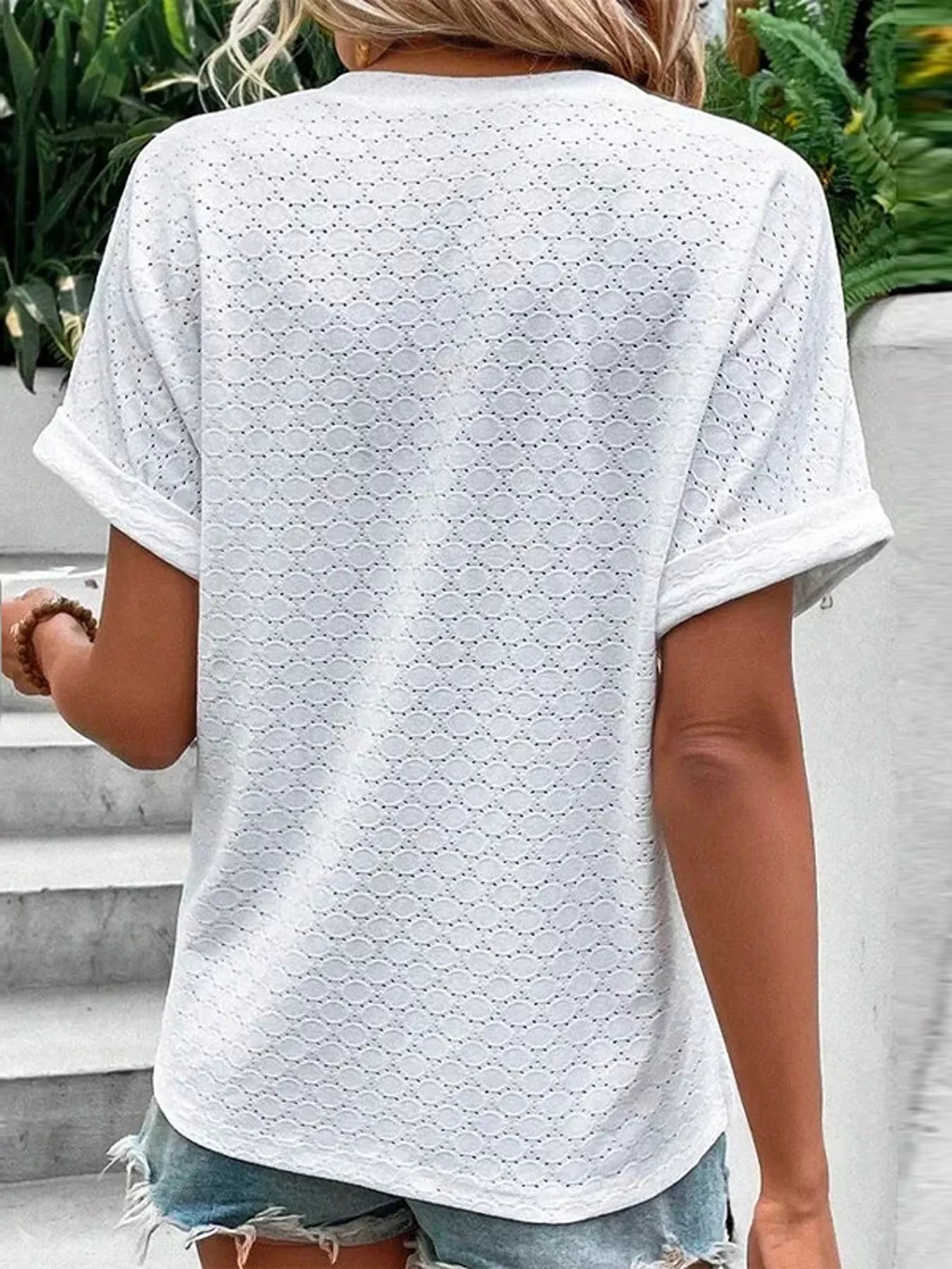 Back view of a white eyelet short-sleeve top with a textured geometric pattern and rolled cuffs