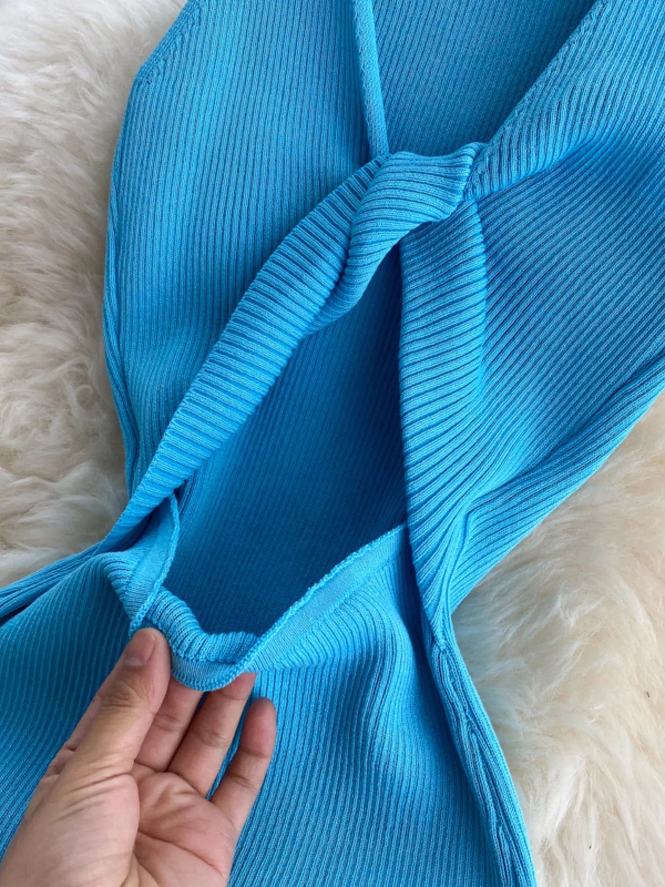 Close detail of knotted open back on bright blue ribbed knit dress held in hand