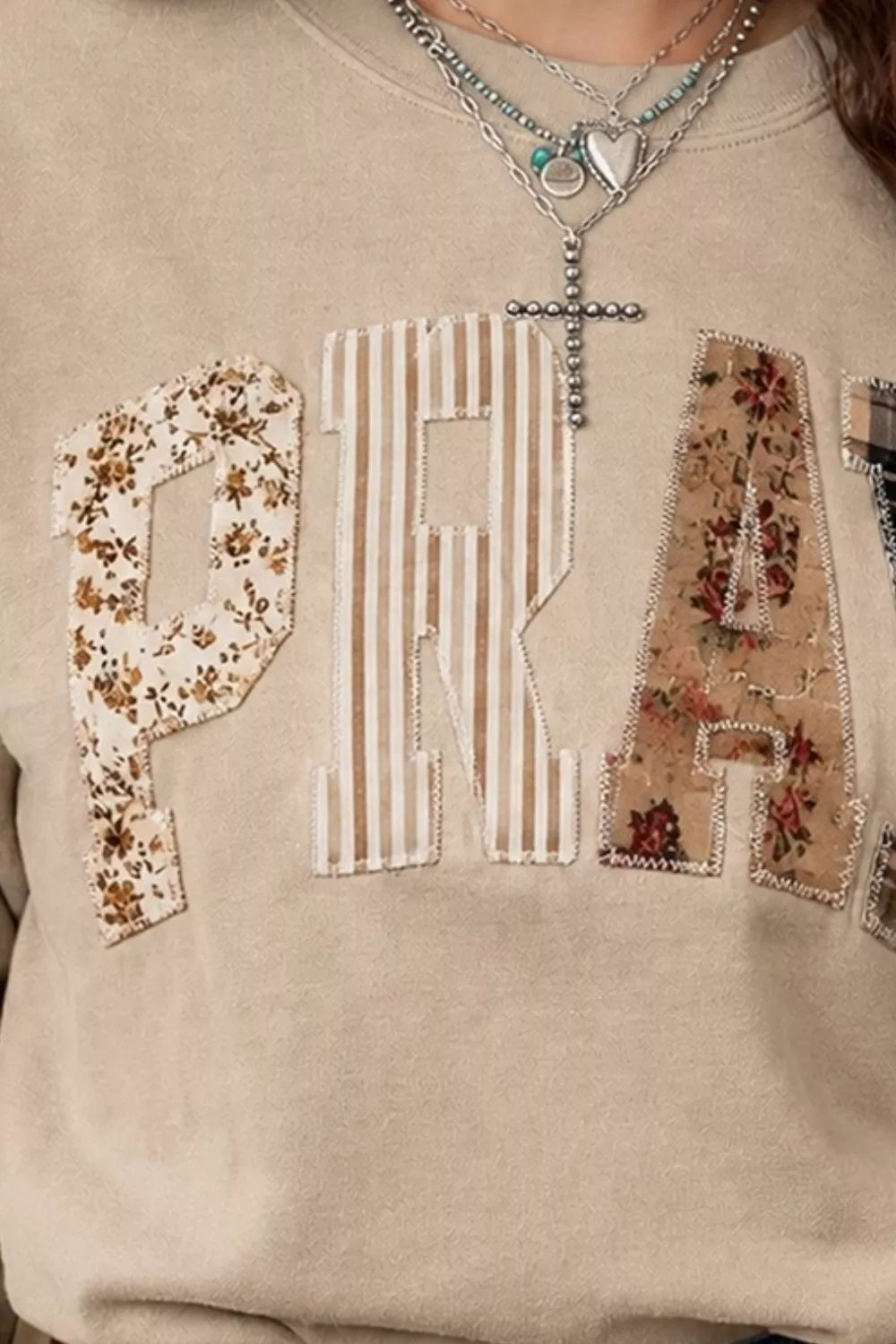 Close detail of khaki western sweatshirt showing floral, striped and plaid patch letters