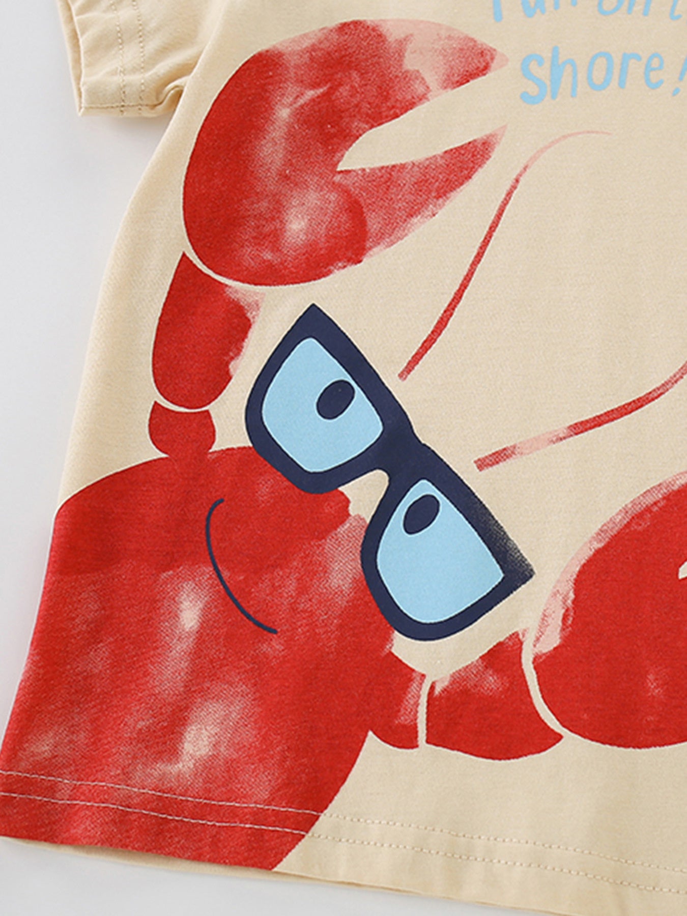 Close-up detail of the red lobster graphic wearing glasses on the apricot children's tee